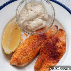 air fryer tilapia with tartar sauce and a lemon wedge.