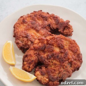 Two golden-brown Southern fried pork chops on a plate with lemon wedges.