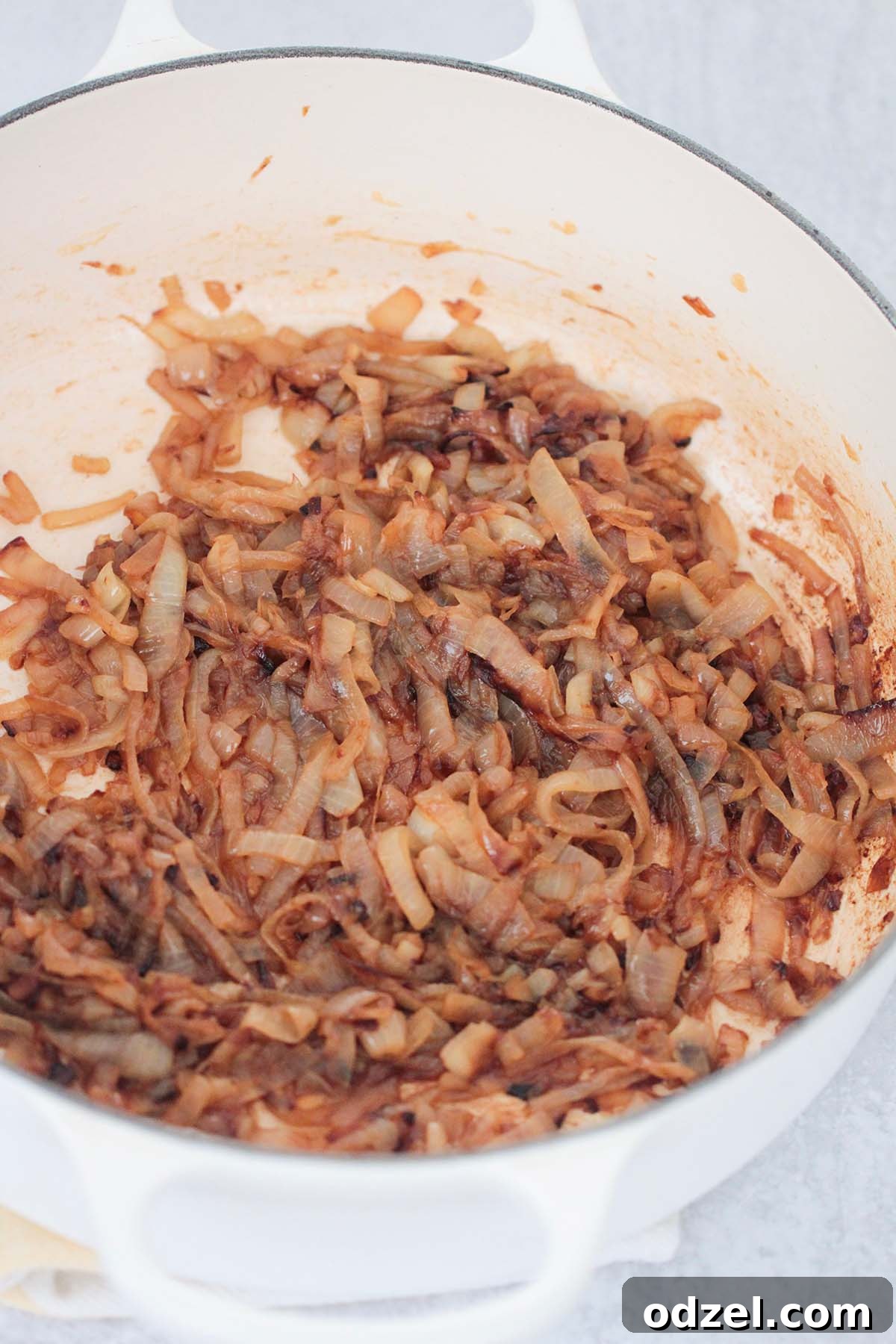 Savory Caramelized Onion Gratin 4 Thinly sliced yellow onions slowly caramelizing in a white Dutch oven on a stovetop, stirring with a wooden spoon.