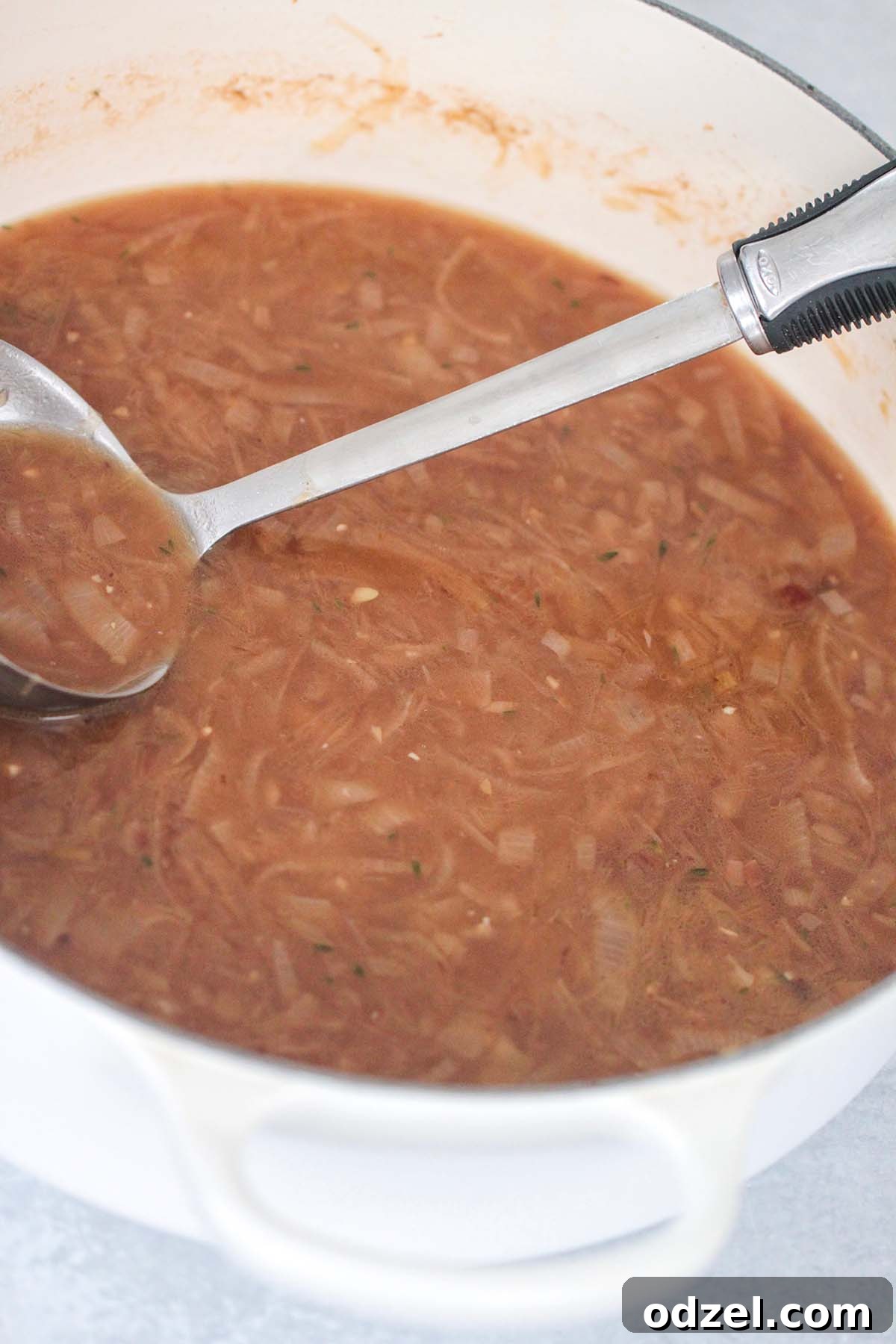 Savory Caramelized Onion Gratin 5 Rich beef broth with caramelized onions and a ladle in a large soup pot, simmering gently.