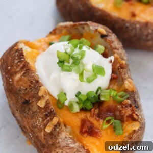 Air fryer loaded baked potatoes up close, showing melted cheese and crispy bacon.