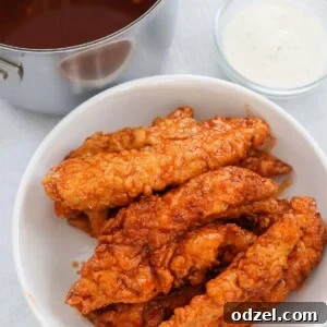 Hot honey chicken tenders on a white plate with sauces on the side.