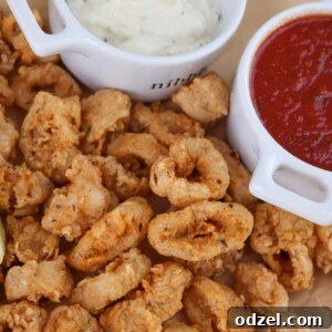 Crispy fried calamari with a lemon wedge, marinara sauce, and tartar sauce on the side.