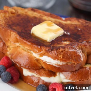 two stuffed french toasts with butter, syrup, and berries.