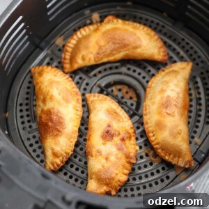 four cooked ground beef empanadas in the air fryer basket.