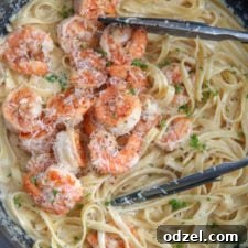 shrimp over fettuccine alfredo in a black skillet with tongs and fresh parsley.