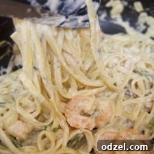 shrimp over fettuccine alfredo in a black skillet with tongs and fresh parsley.