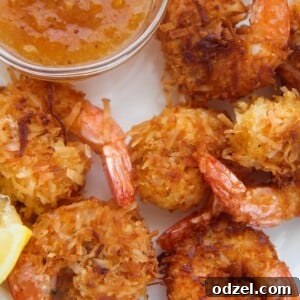 six fried coconut shrimp with orange sauce and lemon wedges on the side.