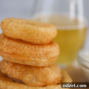 Four beer battered onion rings with a glass of beer in the background.