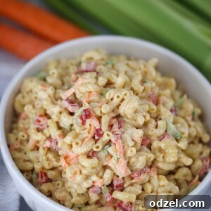 Deli-style macaroni salad in a white bowl with carrots and celery in the background.