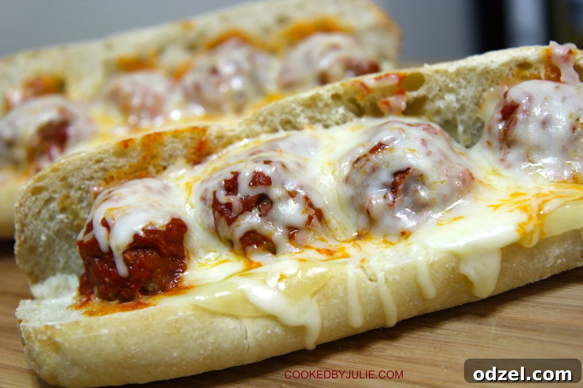 Two deliciously prepared Meatball Parmesan Sandwiches on a wooden board, with melted cheese and rich marinara sauce oozing out.