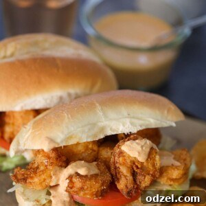 Two crispy shrimp po'boy sandwiches on a wooden board with chips and a pickle on the side.