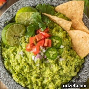 Fresh guacamole in a traditional molcajete, garnished with limes, tomatoes, jalapenos, and surrounded by tortilla chips.