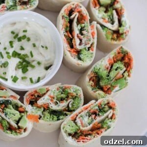 Veggie cream cheese roll-ups neatly arranged on a plate, with a small bowl of cream cheese mixture on the side.