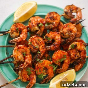 Sizzling BBQ Shrimp Skewers 2 bbq grilled shrimp skewers on a plate with lemon wedges on the side.