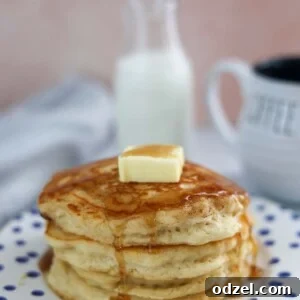 A stack of golden buttermilk pancakes with butter and syrup on top.