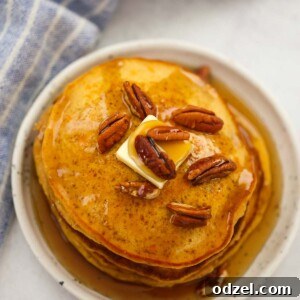 A stack of golden sweet potato pancakes, beautifully garnished with pecans, a melting pat of butter, and a generous drizzle of maple syrup.
