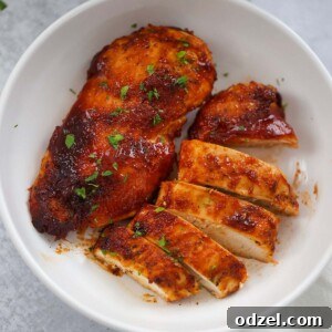 One whole bbq chicken breast and one sliced chicken breast on a plate.