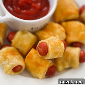 Cooked pigs in a blanket with ketchup on the side.