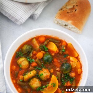 A hearty bowl of vibrant vegetable soup, garnished with fresh herbs, with crusty bread on the side.