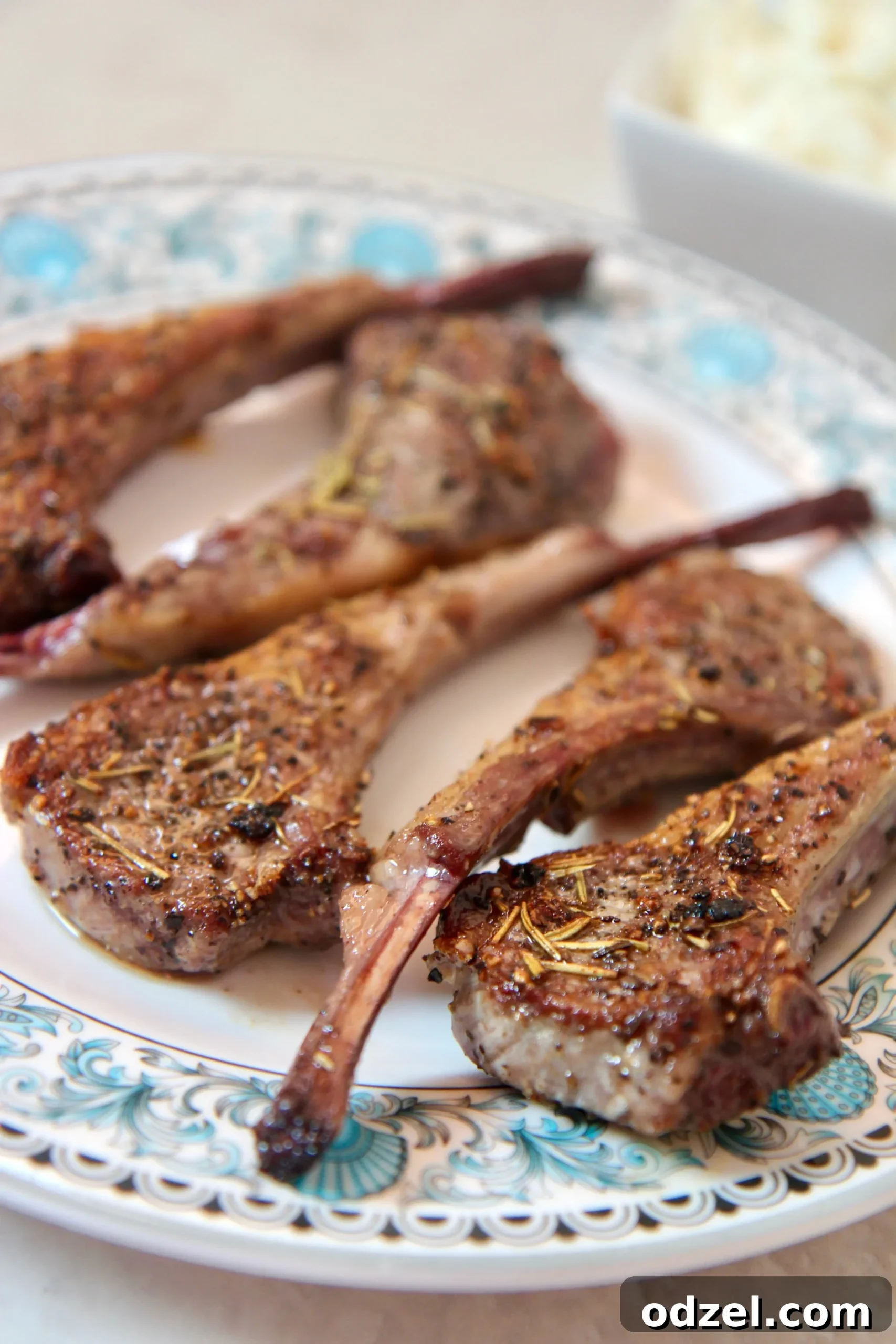 Aromatic Rosemary Garlic Lamb Chops 2 Perfectly seared garlic rosemary lamb chops on a white plate, garnished with fresh rosemary sprigs