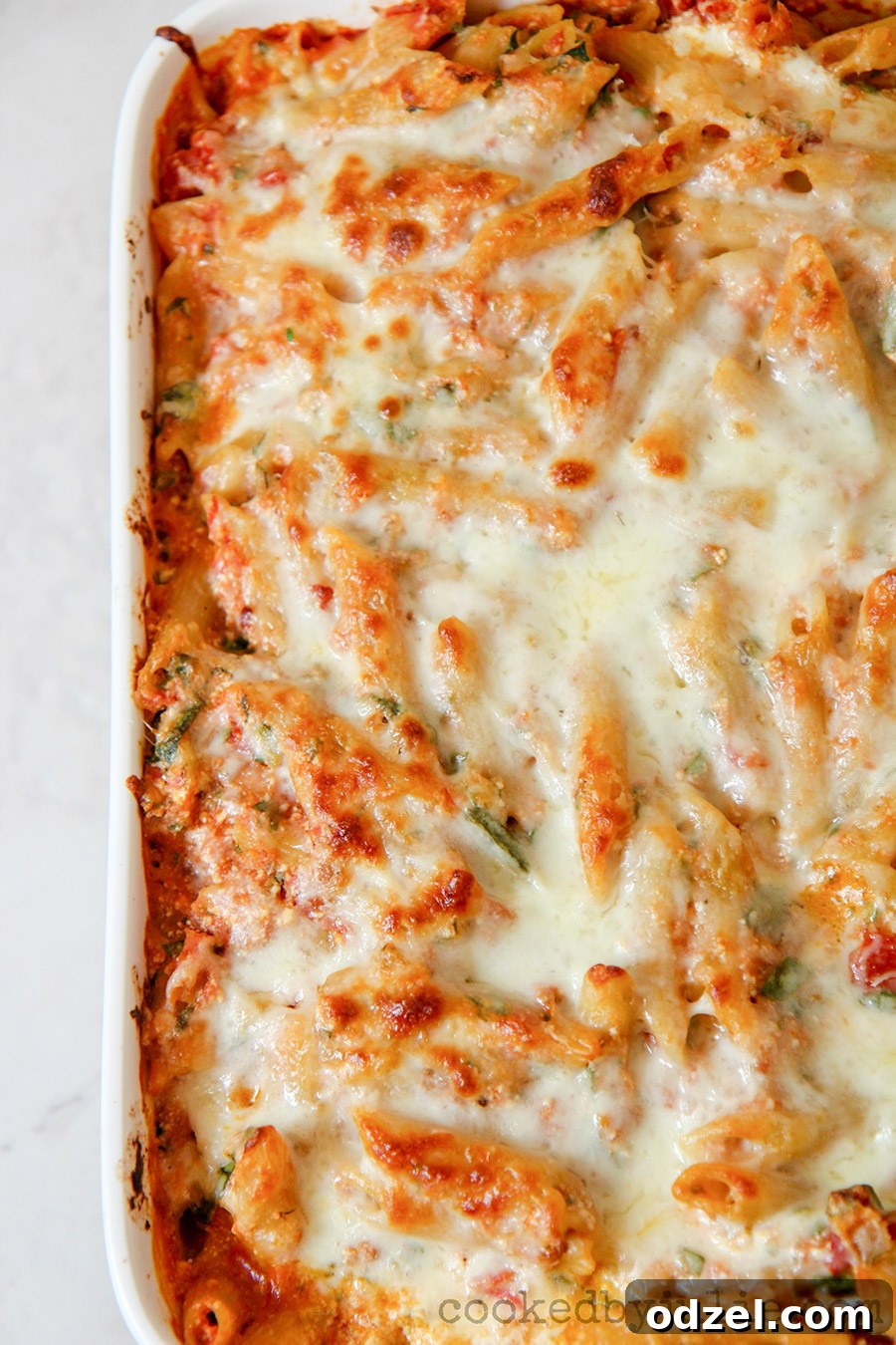 Penne pasta with spinach and cheese in a white casserole dish, close up shot.