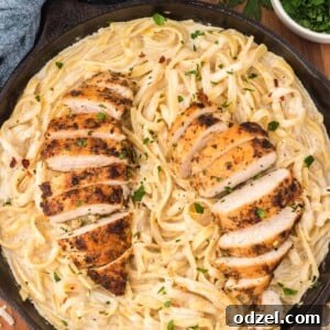 Chicken Fettuccine Alfredo in a black skillet, ready to serve, garnished with red pepper flakes and parmesan.