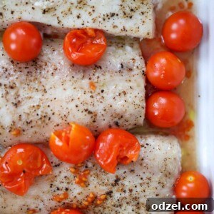 Close-up of baked mahi mahi with burst cherry tomatoes, a slice of lemon, and fresh parsley garnish on a white plate.