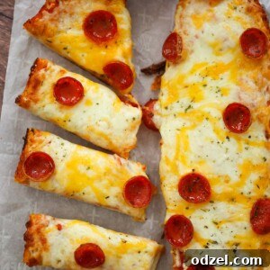 Two French bread pizza loaves with marinara sauce on the side.