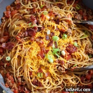 A top-down view of Cowboy Spaghetti in a pot with tongs, showcasing the rich sauce, pasta, and garnishes.