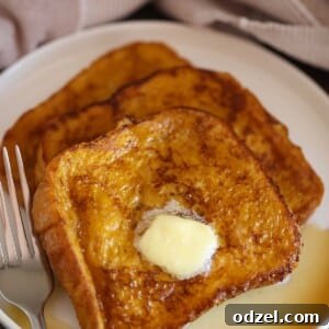 Delicious pumpkin French toast stacks garnished with butter and drizzled with maple syrup on a white plate, ready to be served.