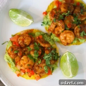 Two shrimp tostadas on a white plate with lime wedges on the side.