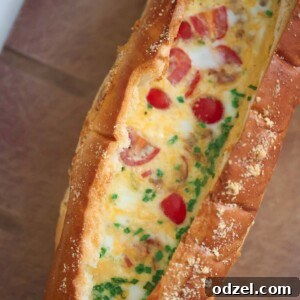 Baked eggs with tomatoes, chives, and cheese inside of a loaf of bread, presented on a wooden board.