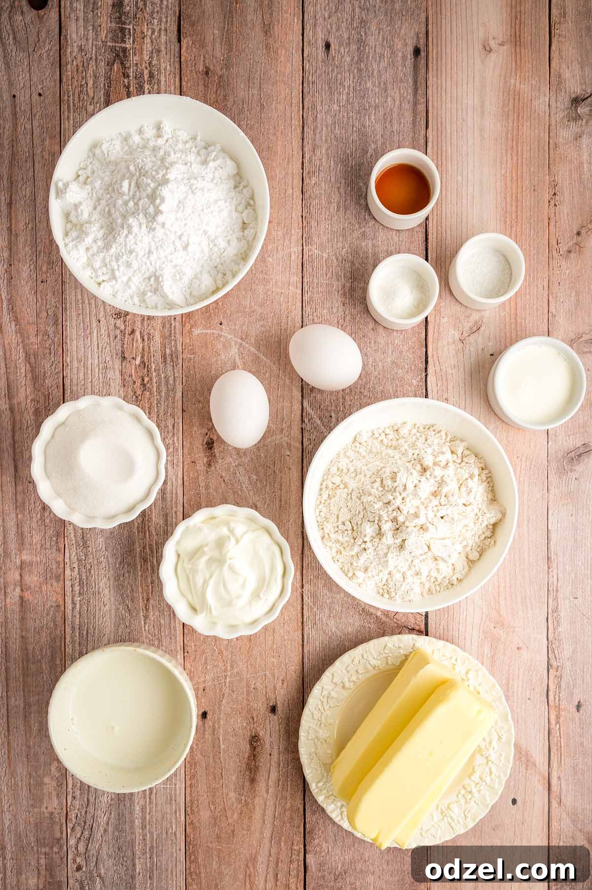 Carefully arranged ingredients for making vanilla cupcakes and vanilla buttercream frosting on a rustic wooden surface.