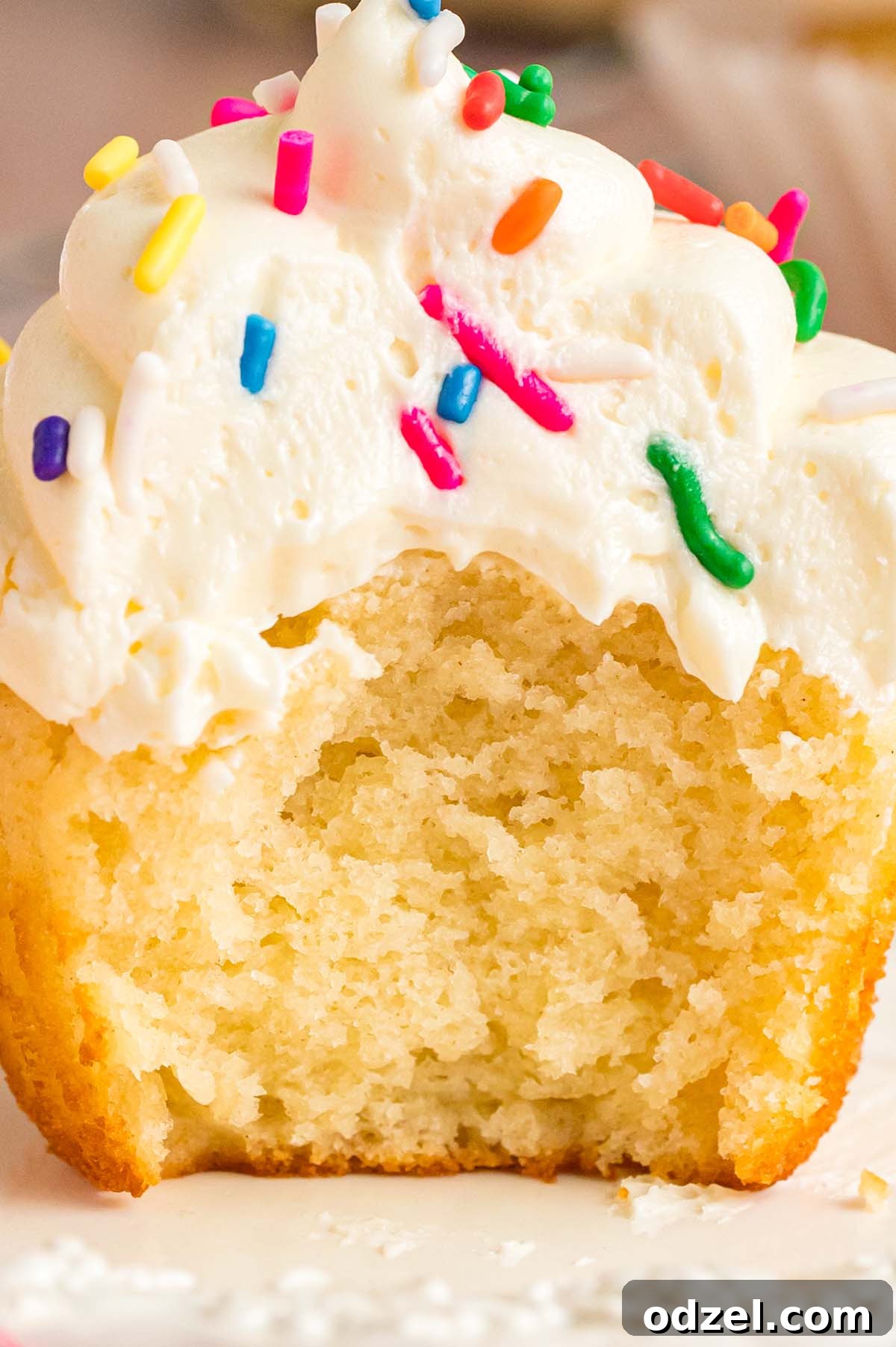 A close-up view of a bitten vanilla cupcake, revealing its fluffy interior and smooth vanilla buttercream frosting.