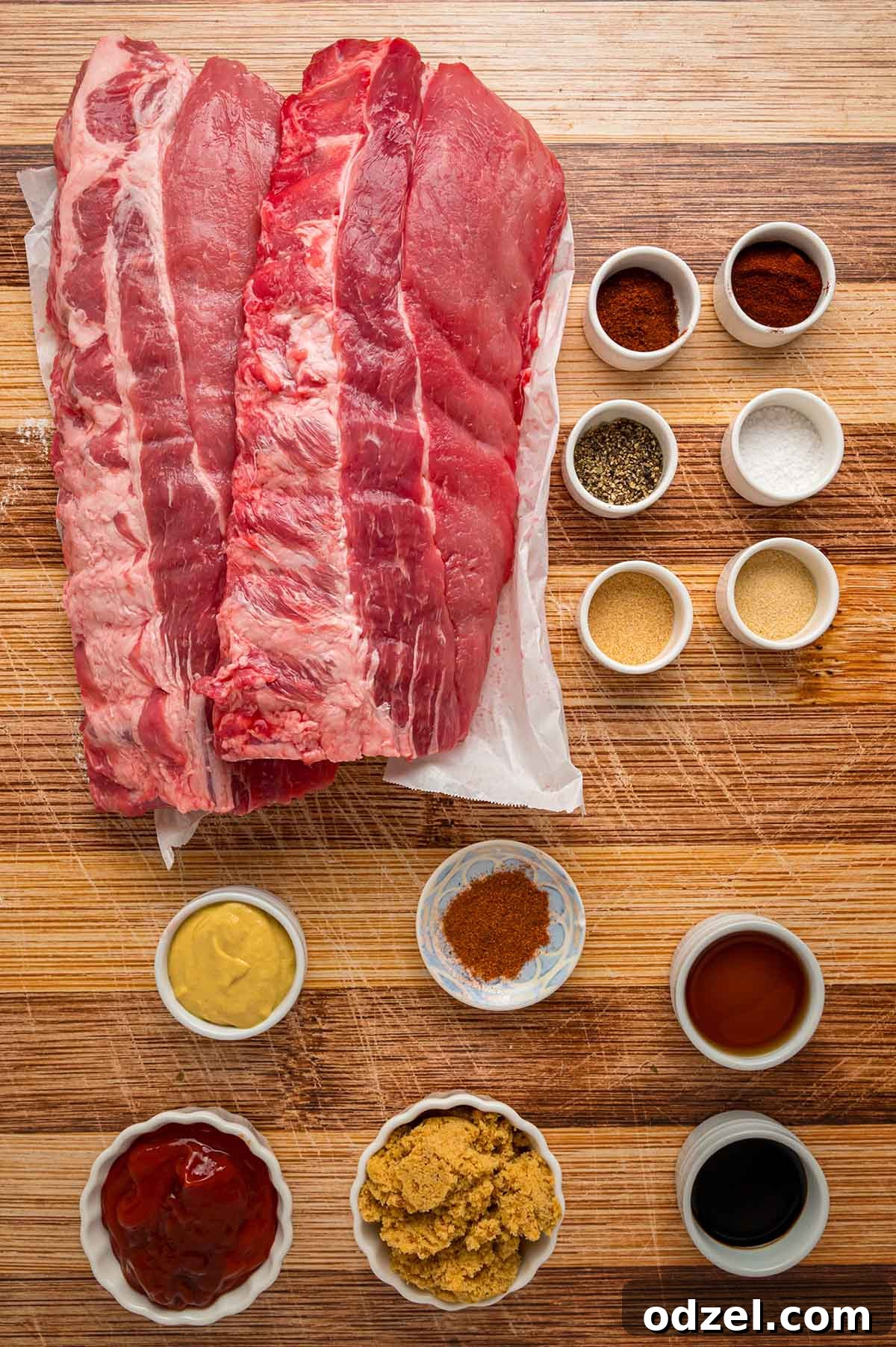 Assortment of fresh ingredients laid out on a wooden board, including baby back ribs, various spices for the rub, and components for homemade BBQ sauce.