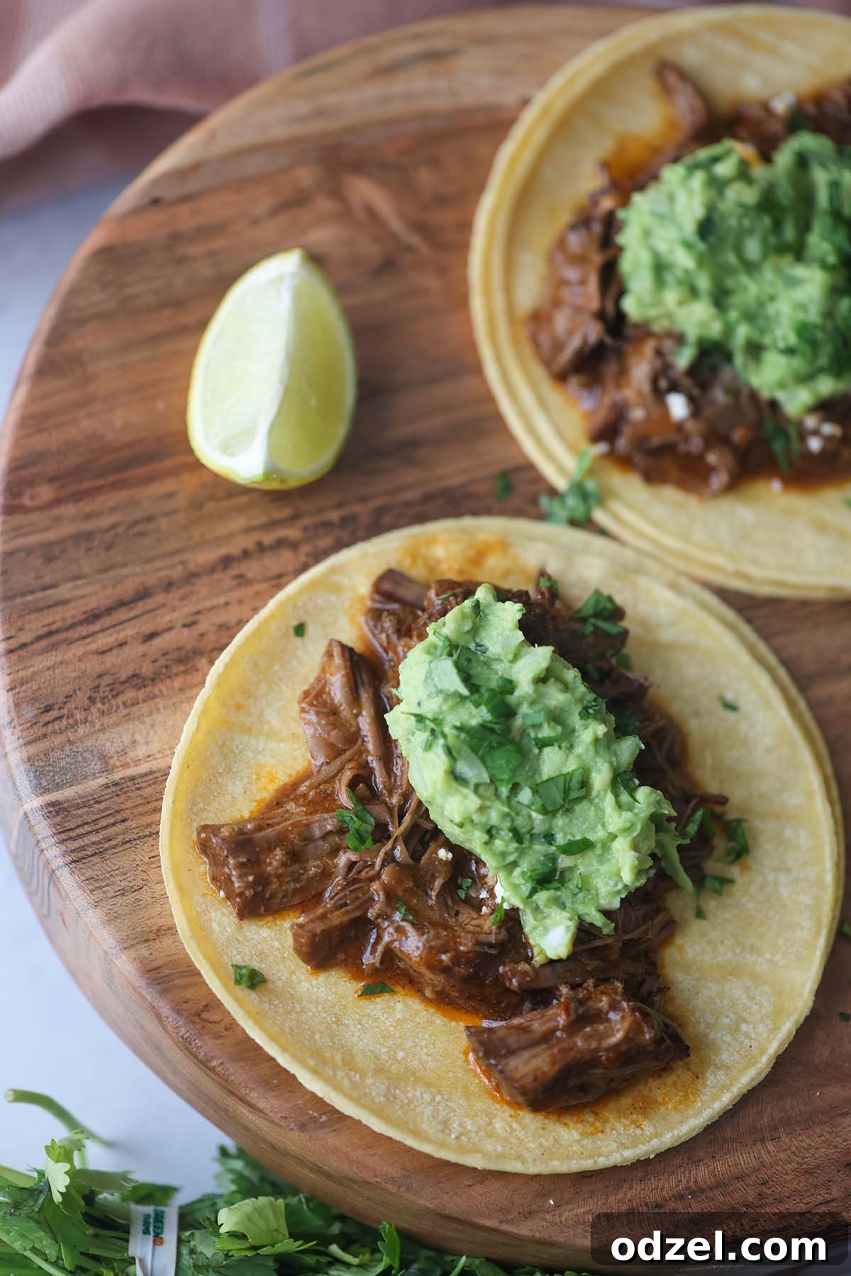 Two vibrant shredded beef tacos on a rustic wooden board, garnished with a fresh lime wedge and ready to be enjoyed. The tacos are generously filled with tender beef and toppings.