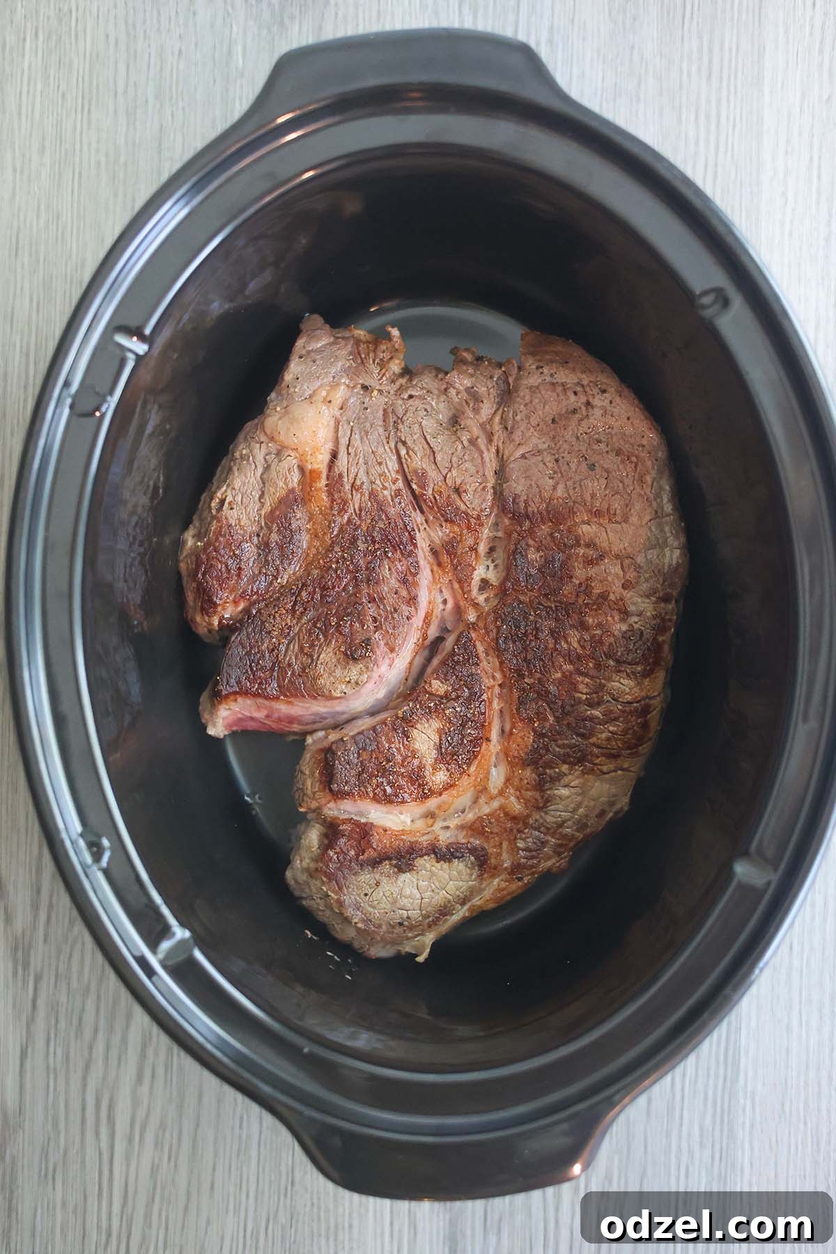 Perfectly seared chuck roast beef nestled in a slow cooker, surrounded by rich sauce and spices, ready to absorb deep flavors over hours.