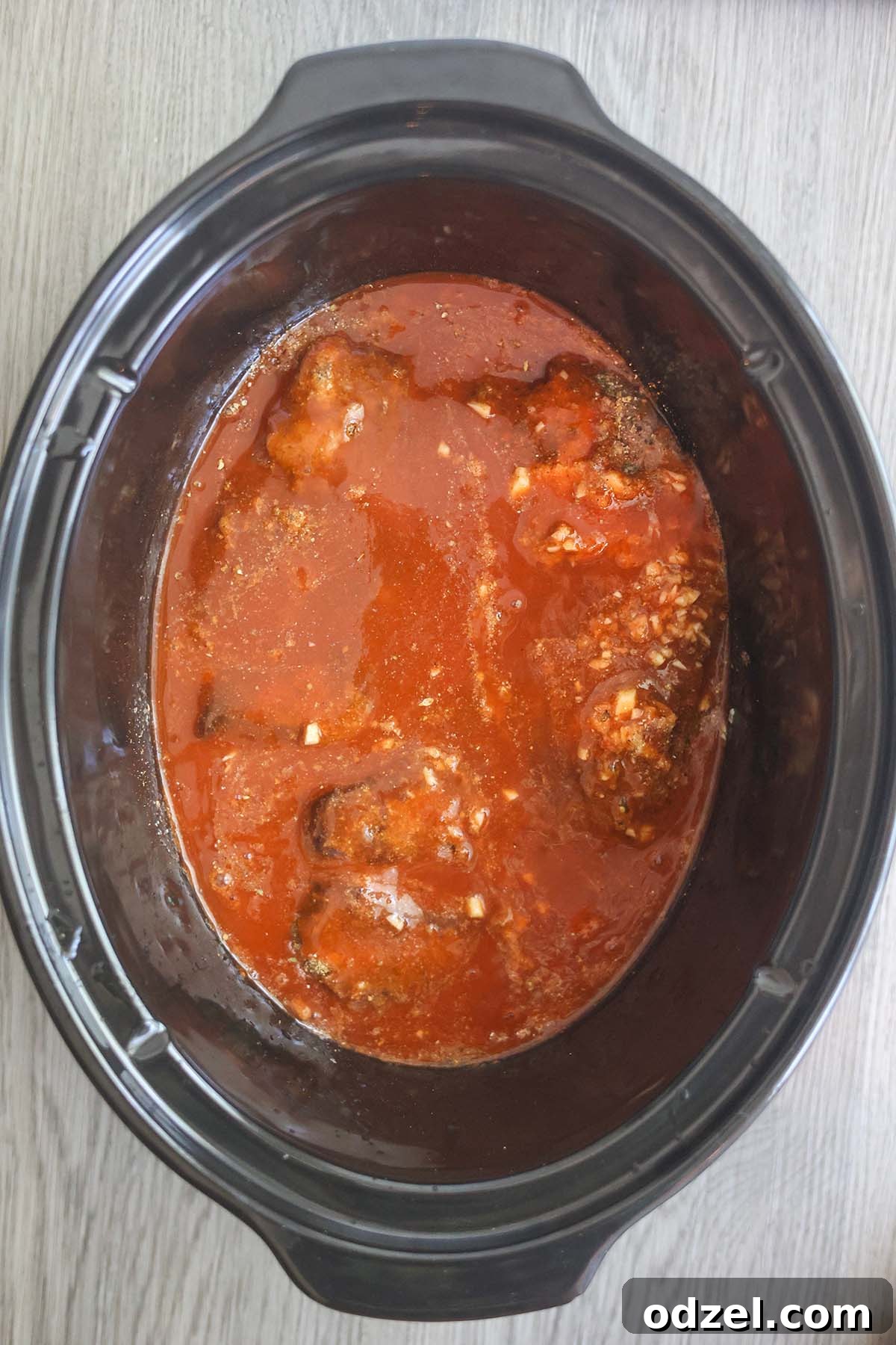 Chuck roast, rich red enchilada sauce, and aromatic spices simmering together in a slow cooker, building deep, complex flavors for tender beef.