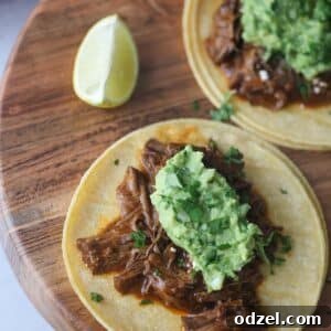 Two shredded beef tacos on a wooden board with a lime wedge on the side.