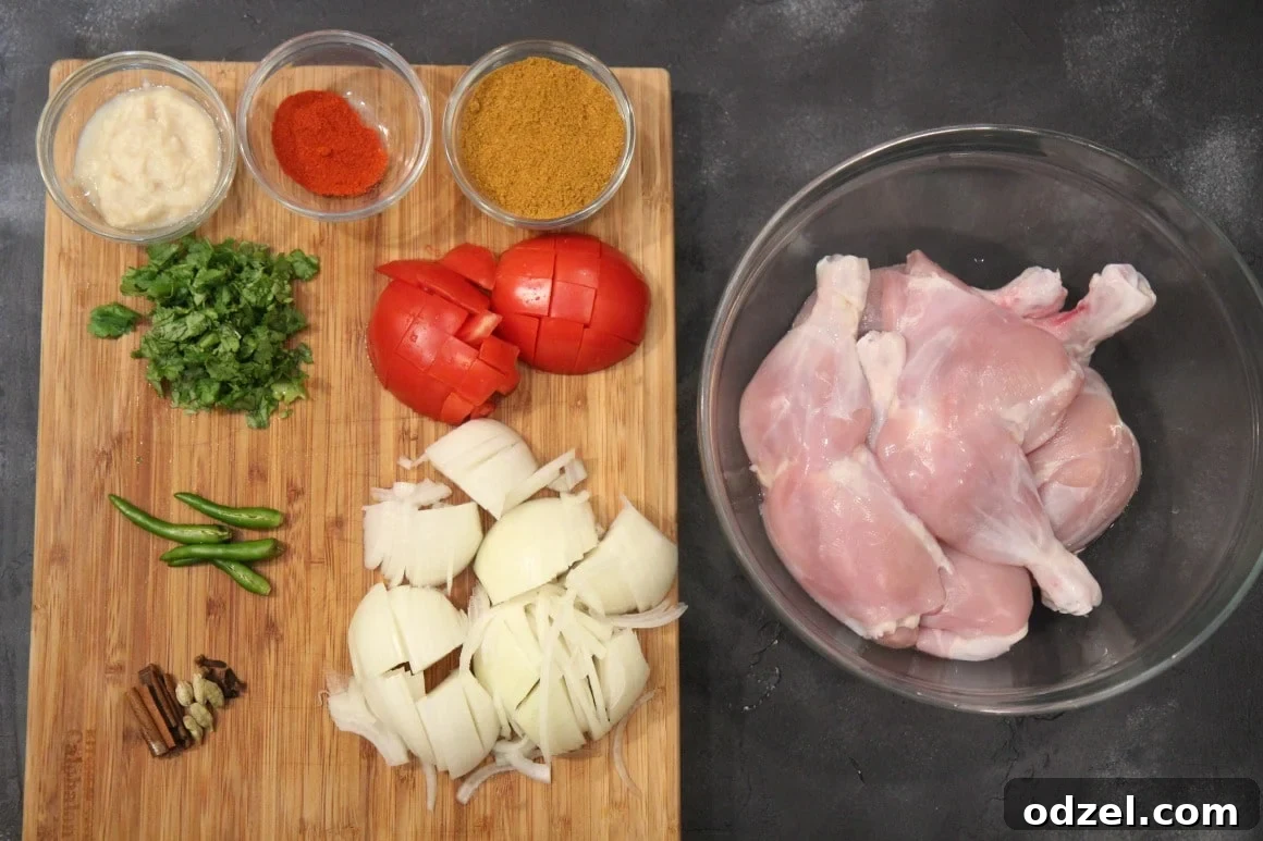 Fresh ingredients for chicken curry including chicken pieces, neatly chopped onions, and ripe tomatoes on a rustic wooden cutting board.