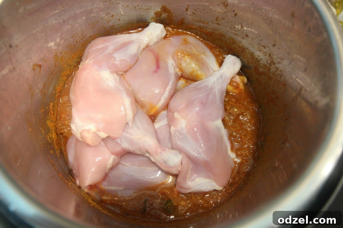 Raw chicken curry ingredients, including chicken pieces, chopped onions, tomatoes, and various spices, layered inside an Instant Pot, ready for cooking.