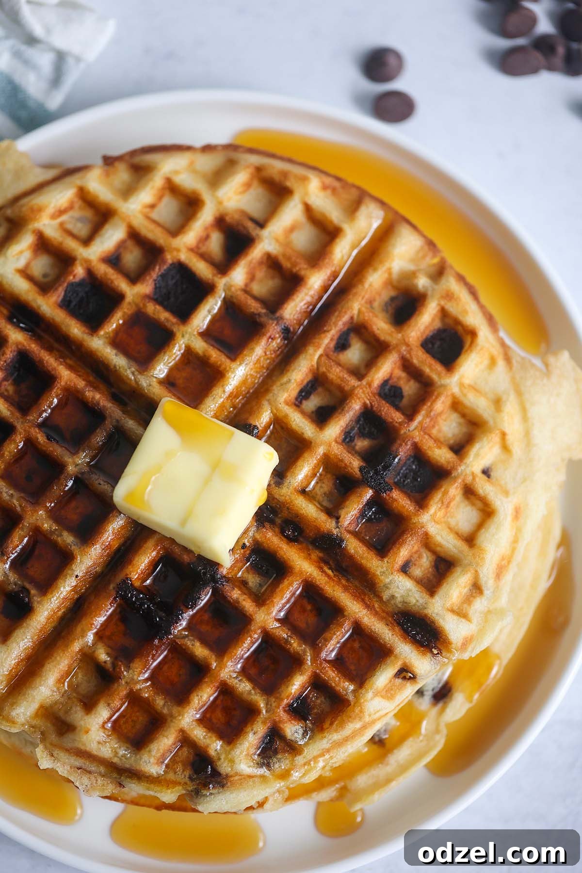 Perfectly golden-brown buttermilk chocolate chip waffle, garnished with melting butter and glistening maple syrup.