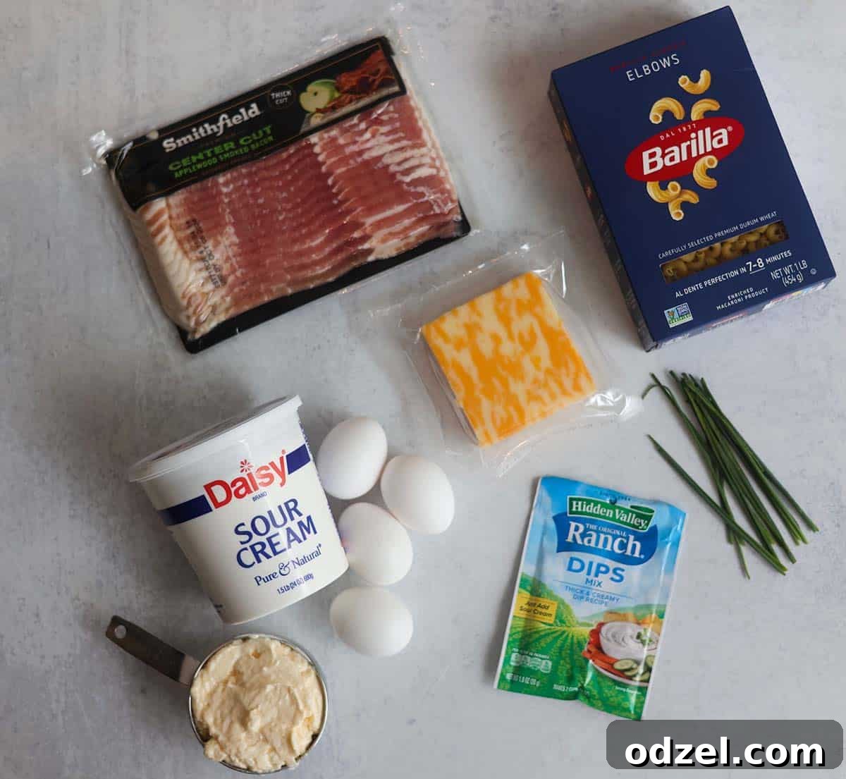 Decadent Bacon Ranch Pasta Salad 3 Individual ingredients for creamy bacon ranch pasta salad laid out: elbow macaroni, shredded cheese, cooked bacon, and fresh chives, ready to be combined.