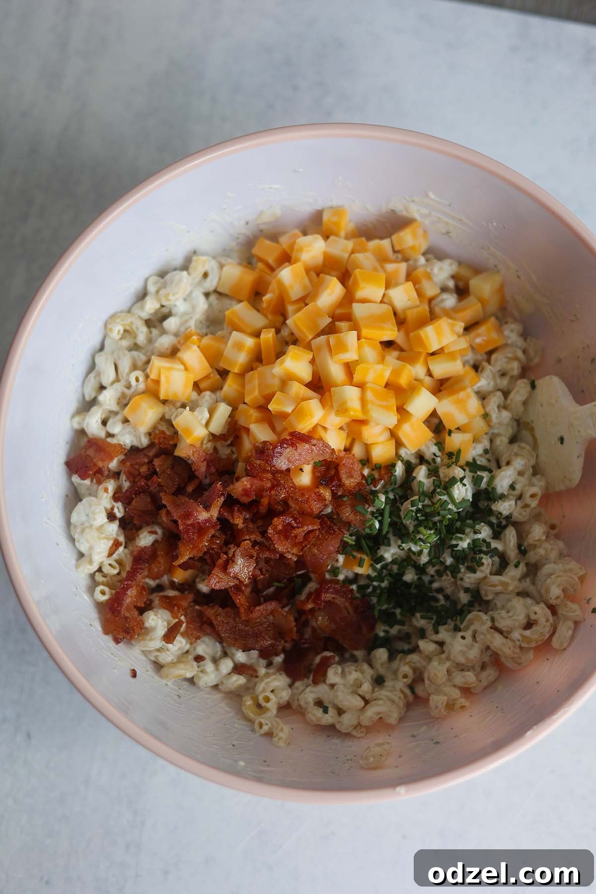 Decadent Bacon Ranch Pasta Salad 4 Cooked macaroni, shredded cheese, crispy bacon bits, and chopped chives combined in a mixing bowl with a spatula, prior to adding the creamy ranch dressing.