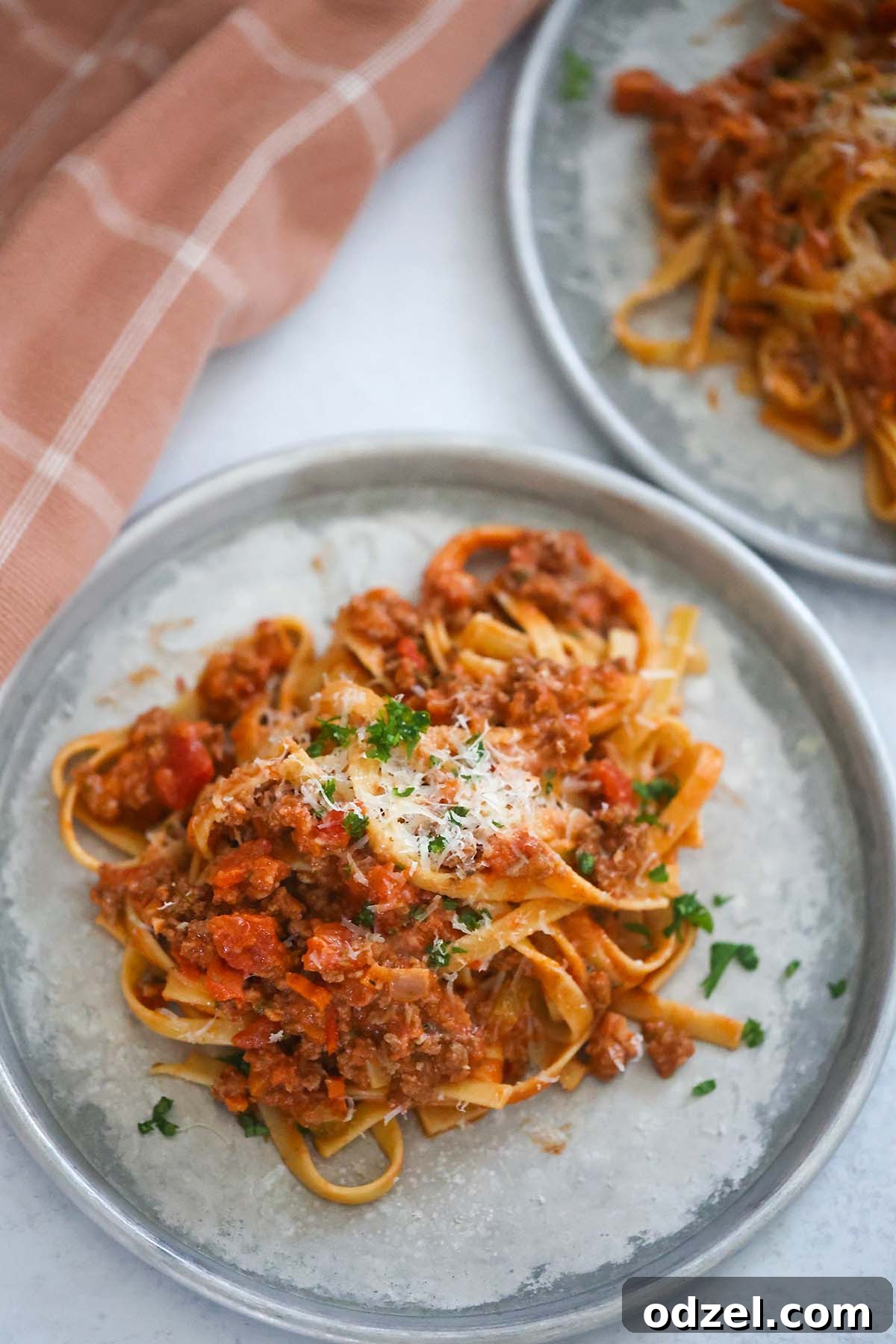Slow-Simmered Bolognese with Fettuccine 2 Two plates of perfectly twirled fettuccine bolognese, garnished with fresh parsley, sitting beside a linen towel.