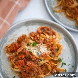 Two plates of fettuccine bolognese with a towel on the side.