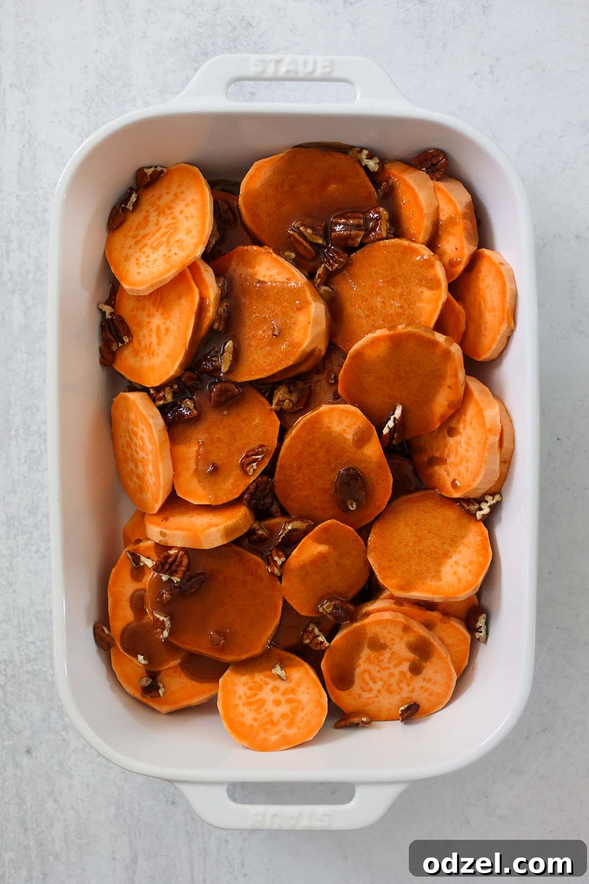Caramelized Bourbon Yams 4 Close-up view of perfectly cooked, glazed yam slices topped with finely chopped pecans, still in the baking dish with rich sauce.