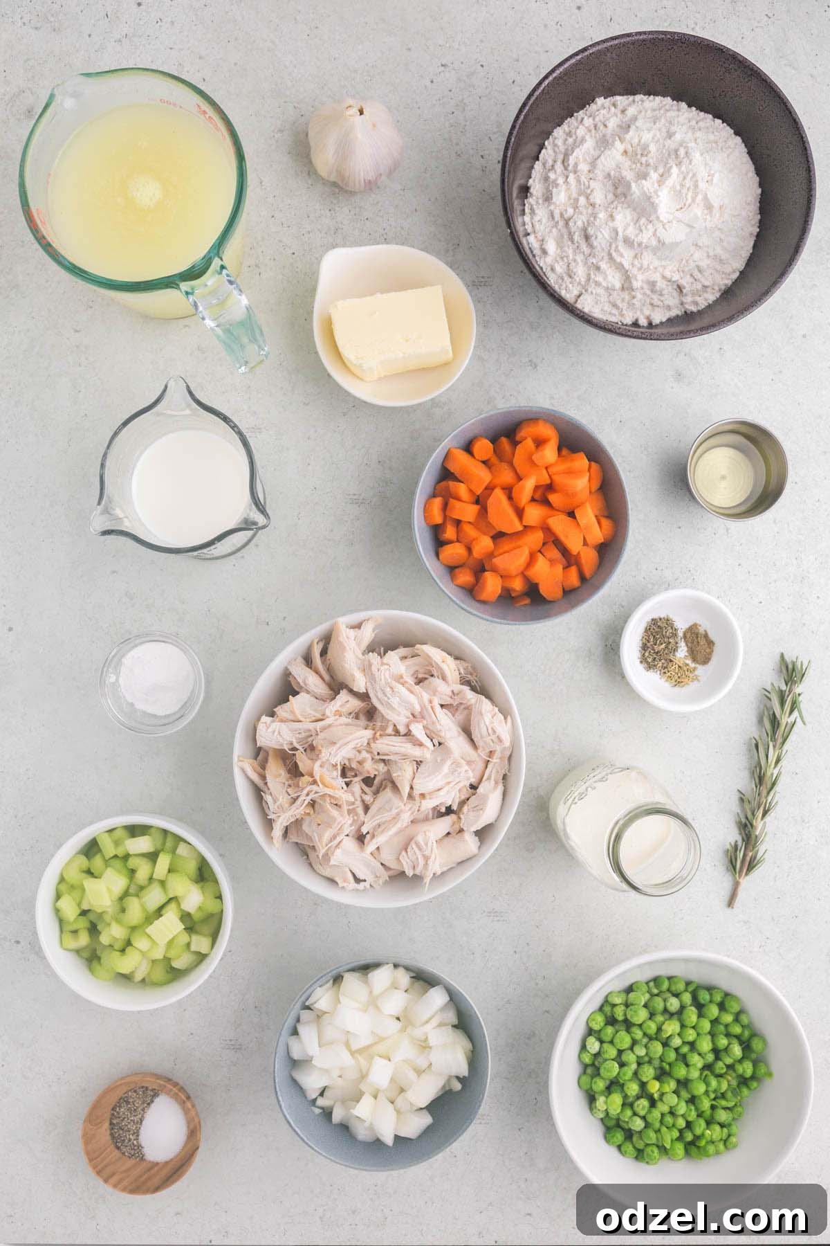 Carefully measured ingredients for chicken and dumplings, including diced vegetables, shredded chicken, fresh herbs, and dry dumpling ingredients, laid out on a clean gray kitchen surface, ready for preparation.