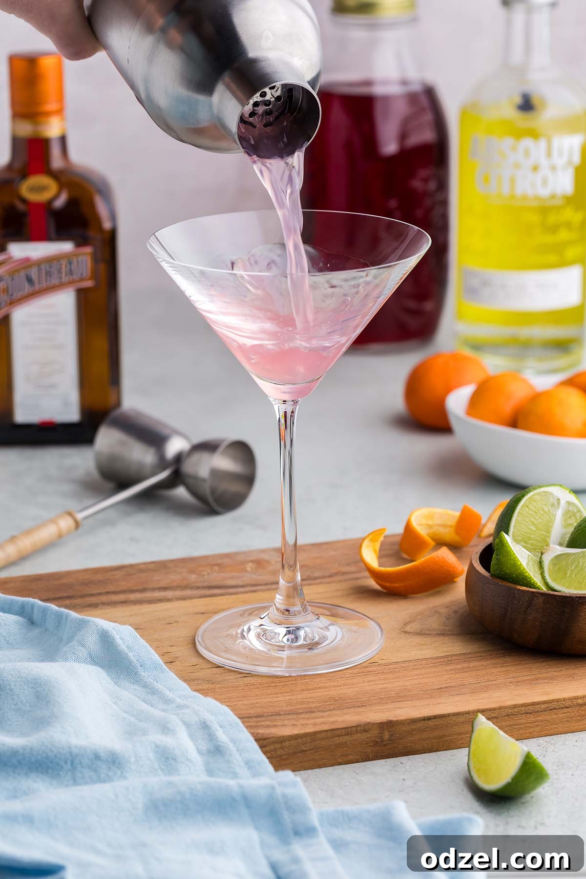 A cocktail shaker in action, skillfully pouring a freshly mixed Cosmopolitan into a waiting martini glass, showcasing the perfect light pink color.